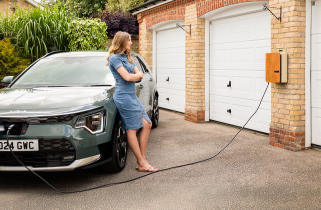 Femme et sa voiture électrique devant une borne de recharge à la maison