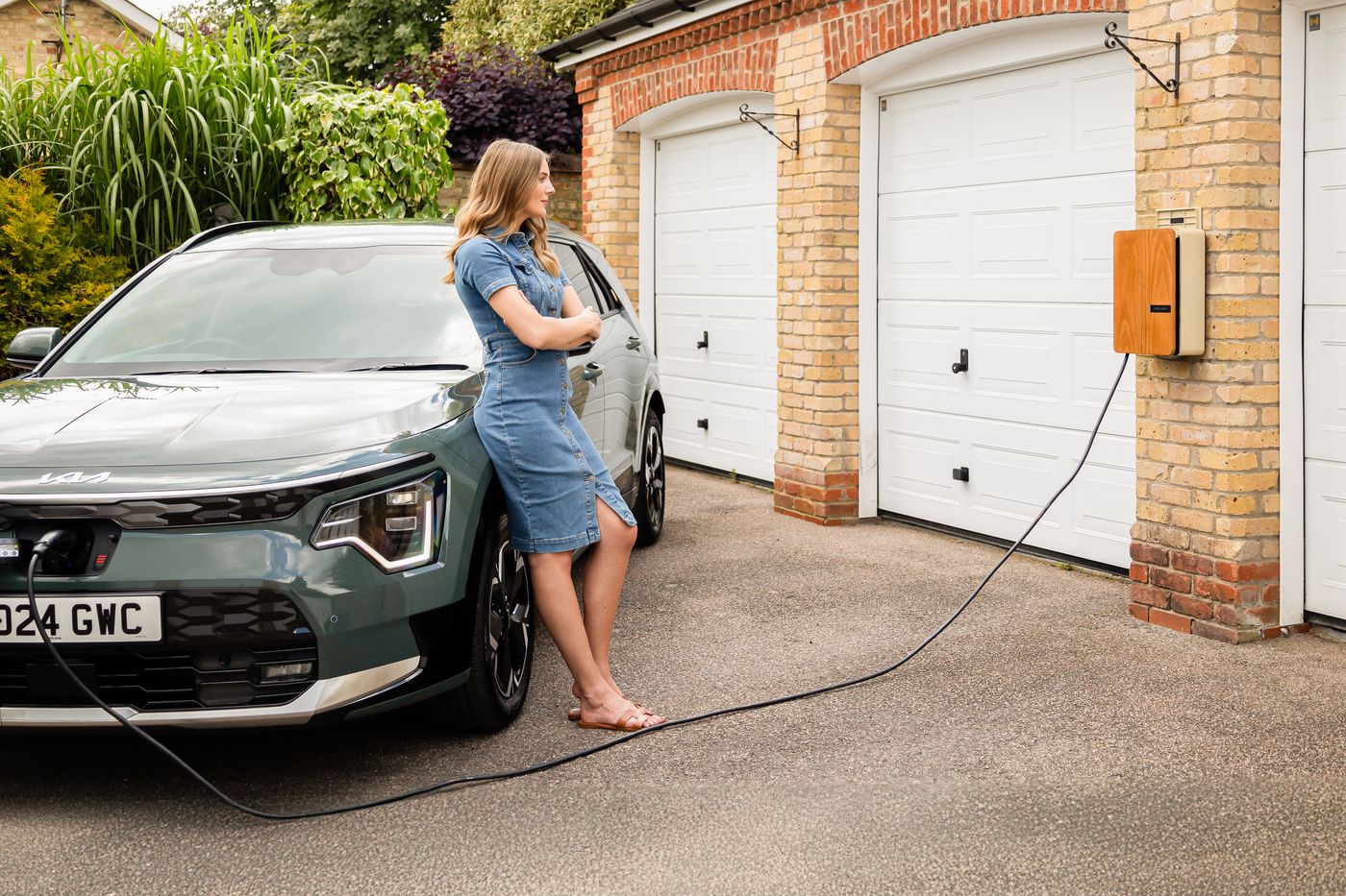 Femme et sa voiture électrique devant une borne de recharge à la maison